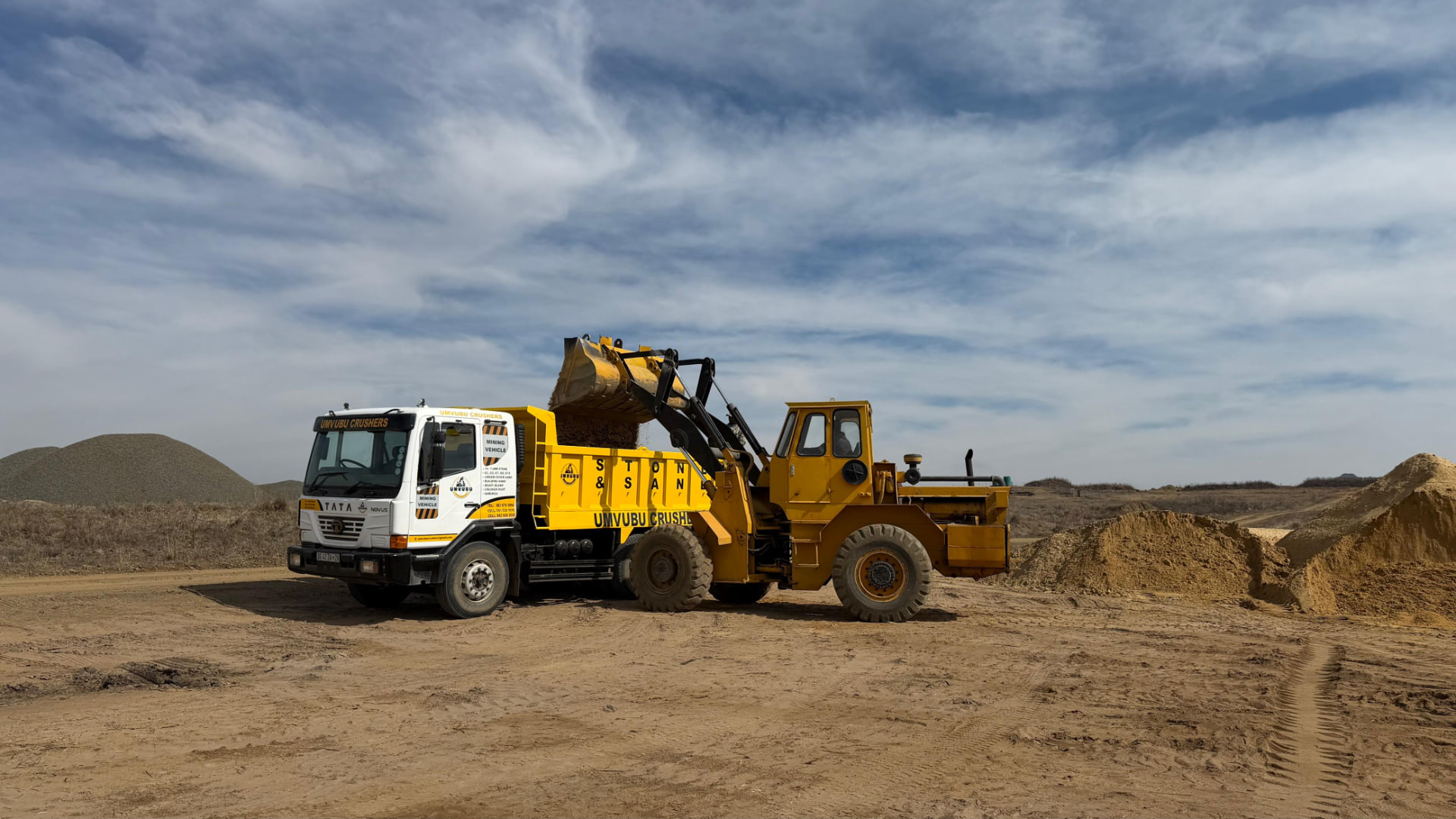 Front-end loader filling a branded Umvubu Crushers tipper truck at the quarry