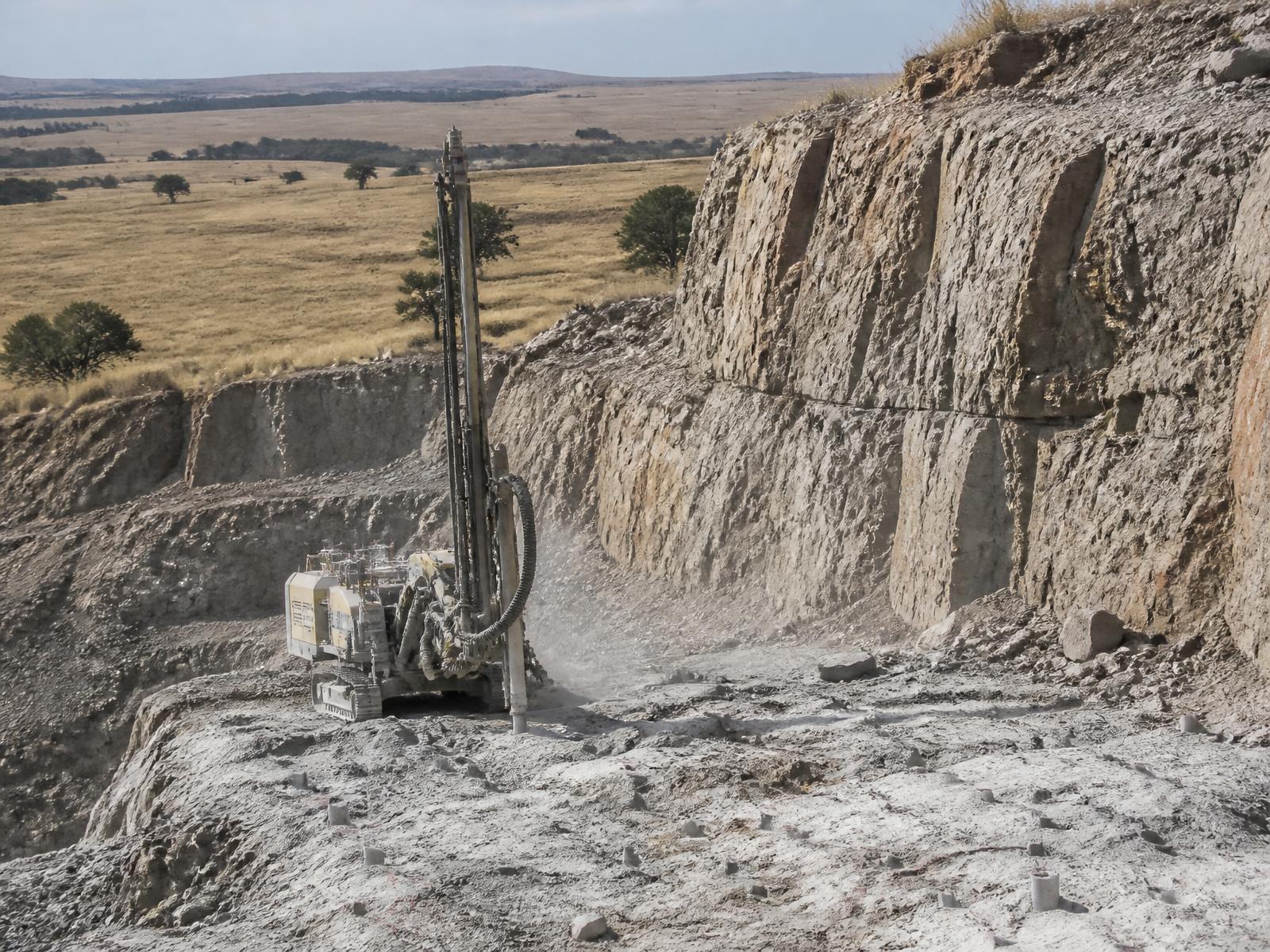 Drilling rig preparing a quarry rock face with grassland behind